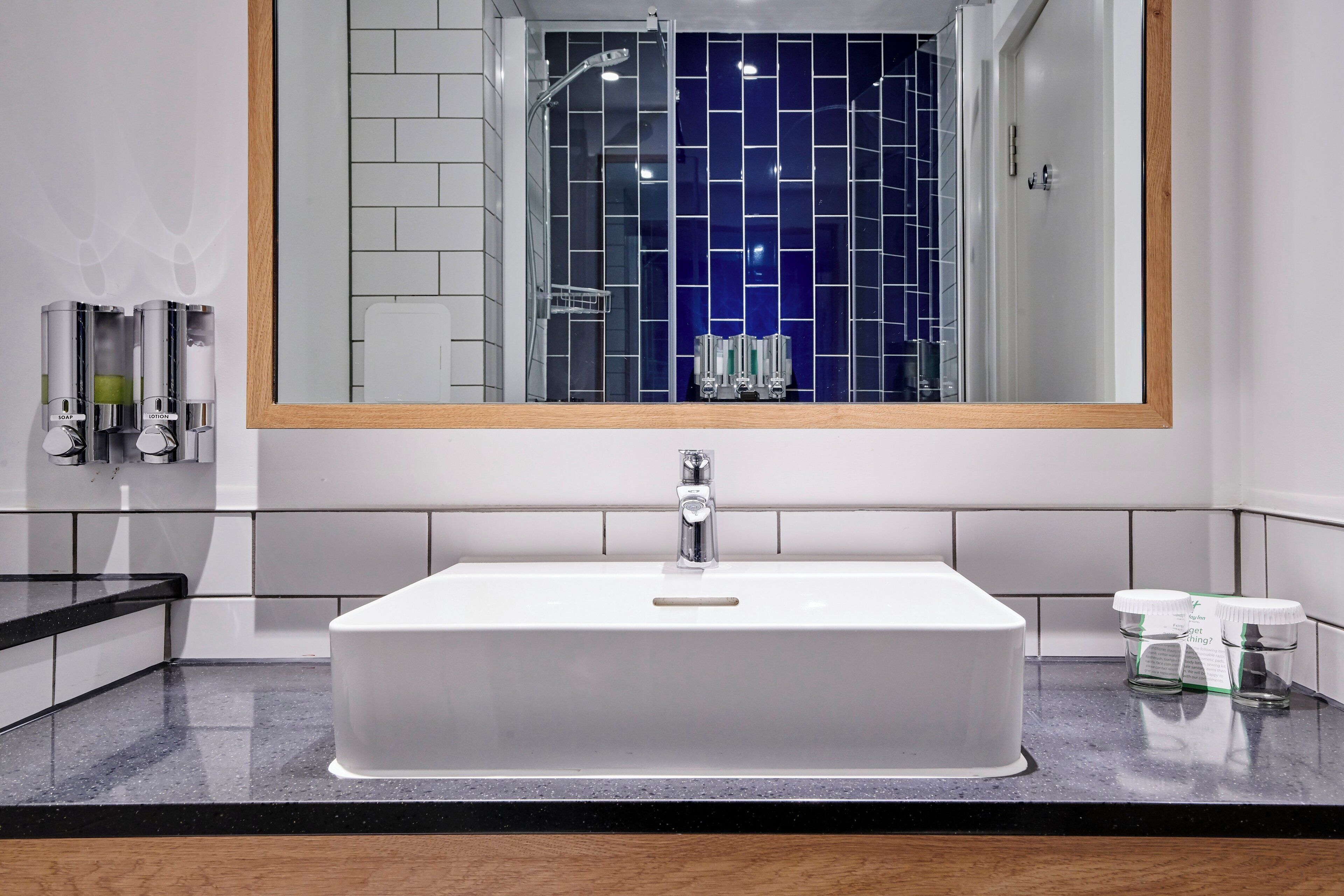 Ein Badezimmer mit einem rechteckigen Waschbecken, einem Spiegel und einer gefliesten Wand.