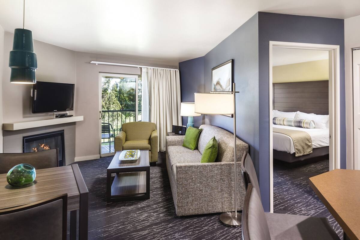 A hotel room with a sofa, armchair, TV, fireplace, and a bed.