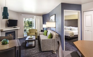 Habitación de hotel con sofá, sillón, televisión, chimenea y cama.