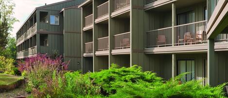 A multi-story building with balconies and a garden area in front.