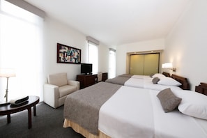 A hotel room with two beds, a desk, a chair, a television, and a painting on the wall.