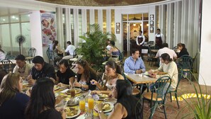 A restaurant with diners seated at tables, a large plant in the center, and a ceiling mural. - Hotel Continental (Guayaquil)