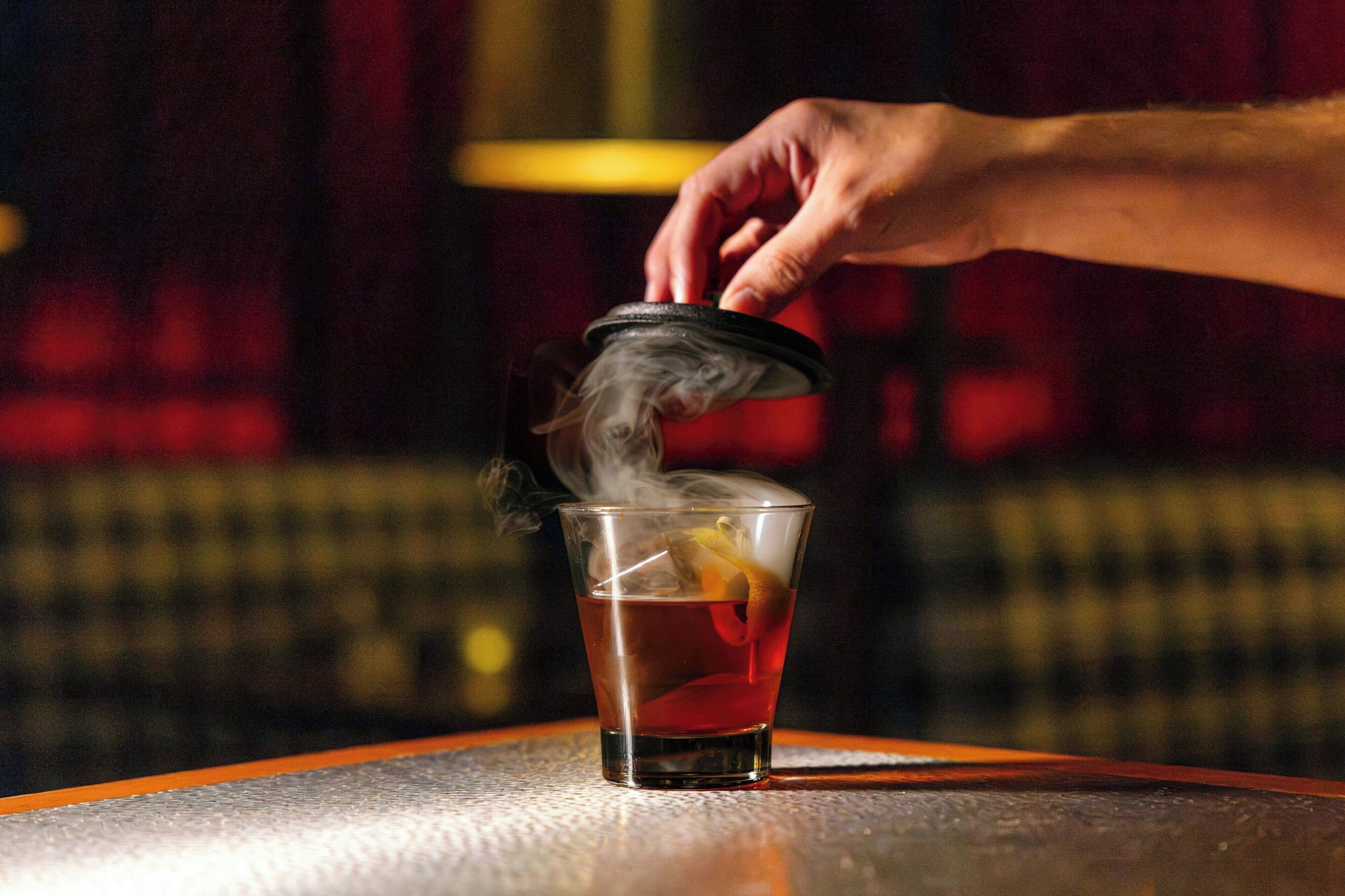 A hand pouring a drink into a glass with a lid on the table.