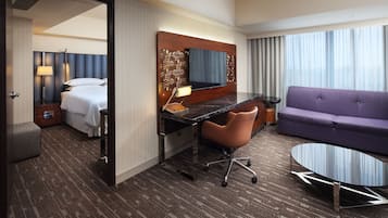 A hotel room with a bed, desk, chair, sofa, and a TV.