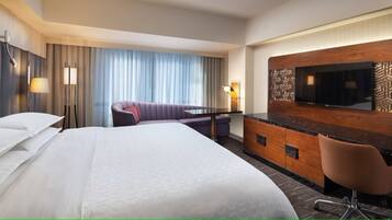 Een hotelkamer met een groot bed, een bank, een bureau met een flatscreen televisie en een minibar.