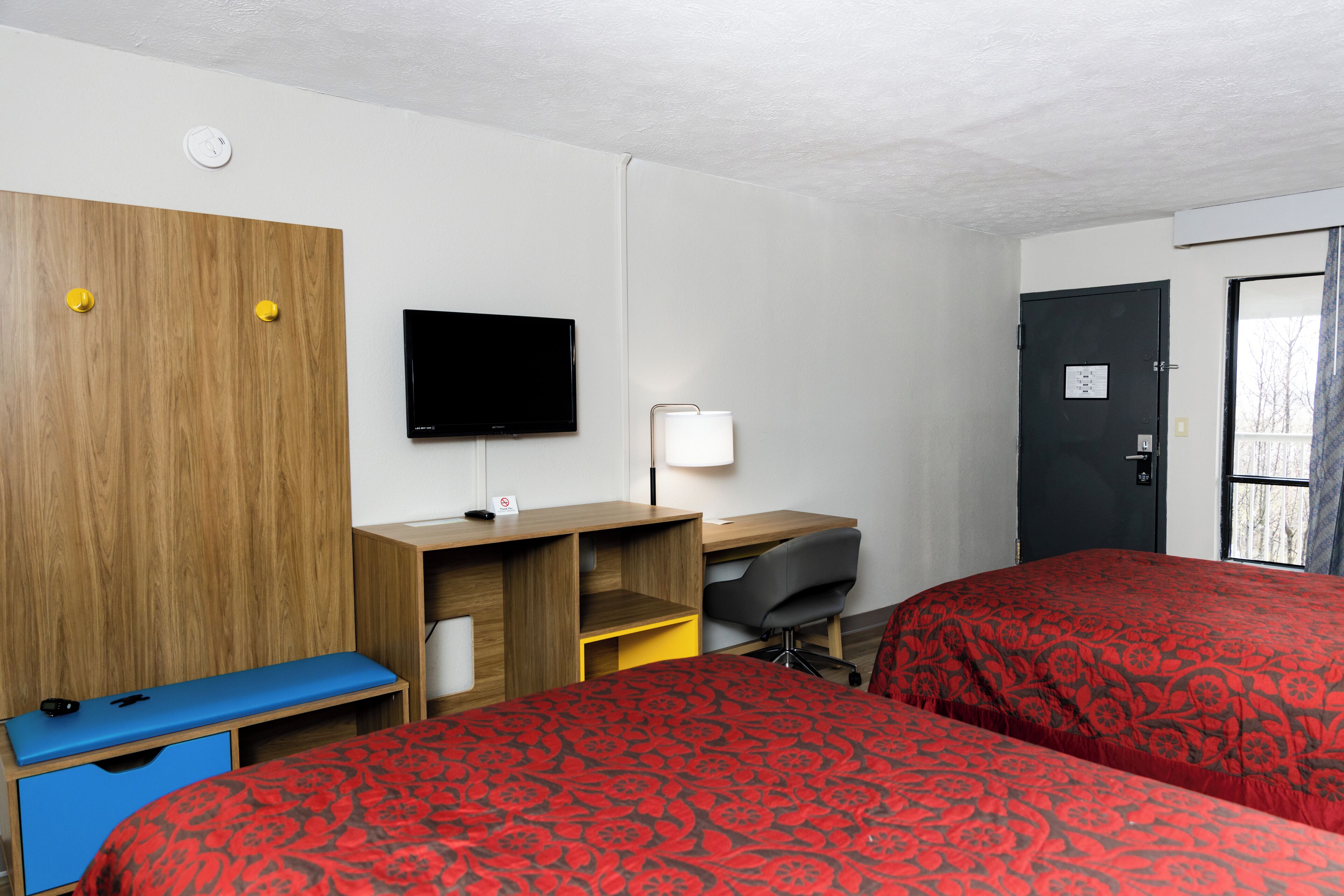 A hotel room with two beds, a desk, a TV, and a window with curtains.
