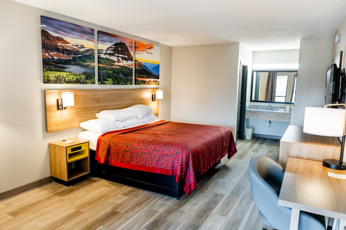 Ein Hotelzimmer mit Bett, Schreibtisch, Stuhl und einem Kunstwerk an der Wand.