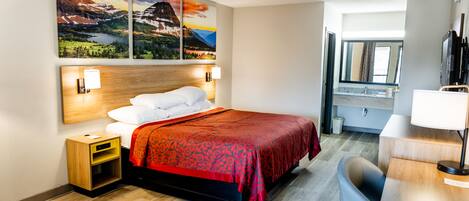 A hotel room with a bed, a desk, a chair, and artwork on the wall.