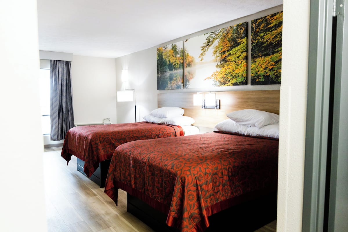 Ein Hotelzimmer mit zwei Betten, einem großen Fenster mit Vorhängen und einem Wandbild.