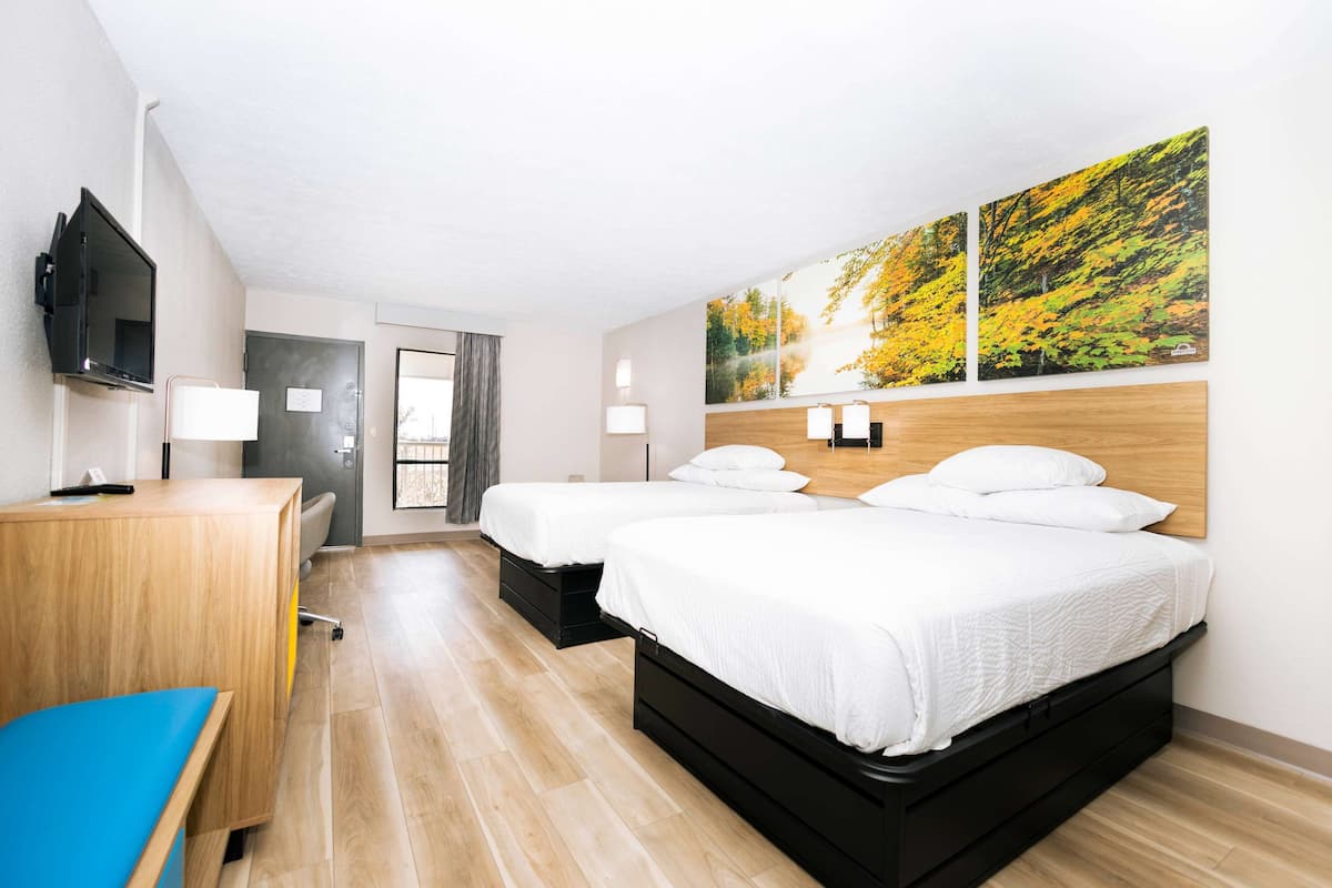 Ein Hotelzimmer mit zwei Betten, einem Schreibtisch, einem Fernseher und einem großen Fenster.