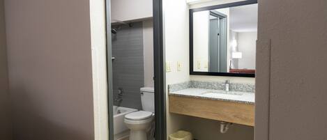 A bathroom with a toilet, sink, mirror, and shower.
