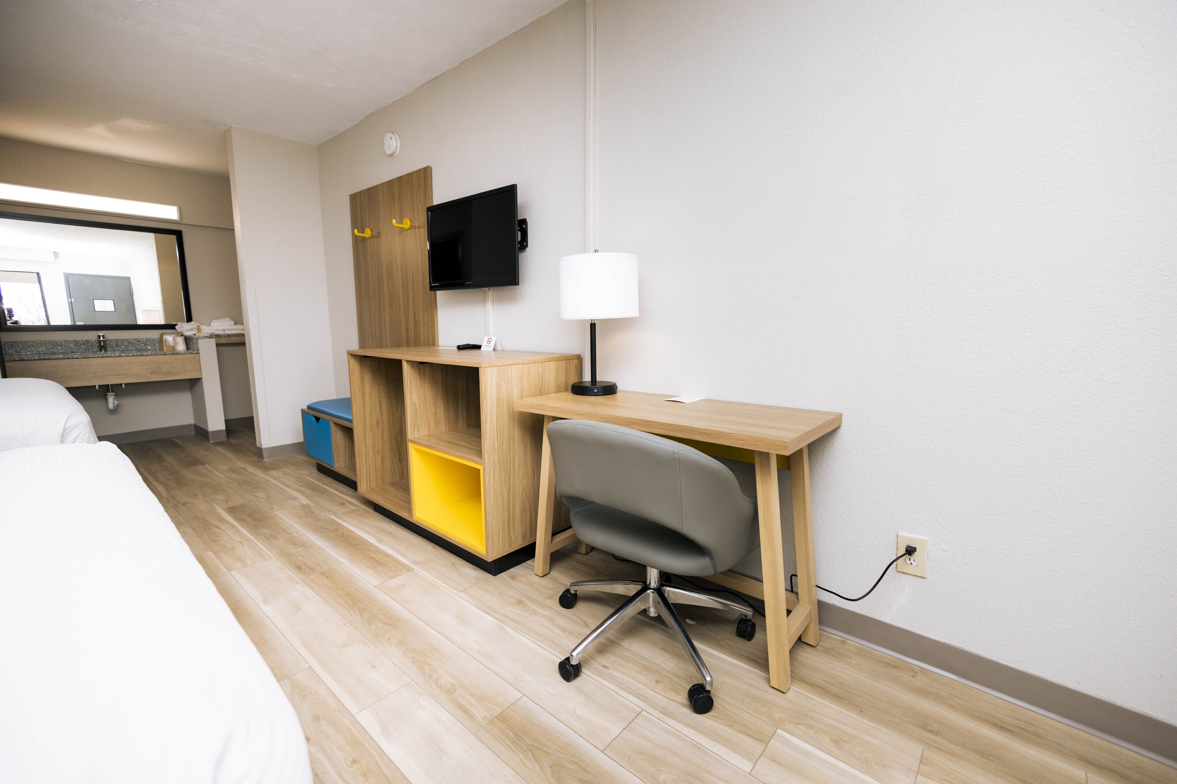 A hotel room with a bed, a desk with a chair, a TV, and a lamp.