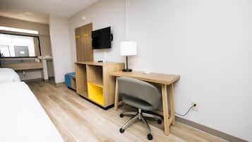 A hotel room with a bed, a desk with a chair, a TV, and a lamp.