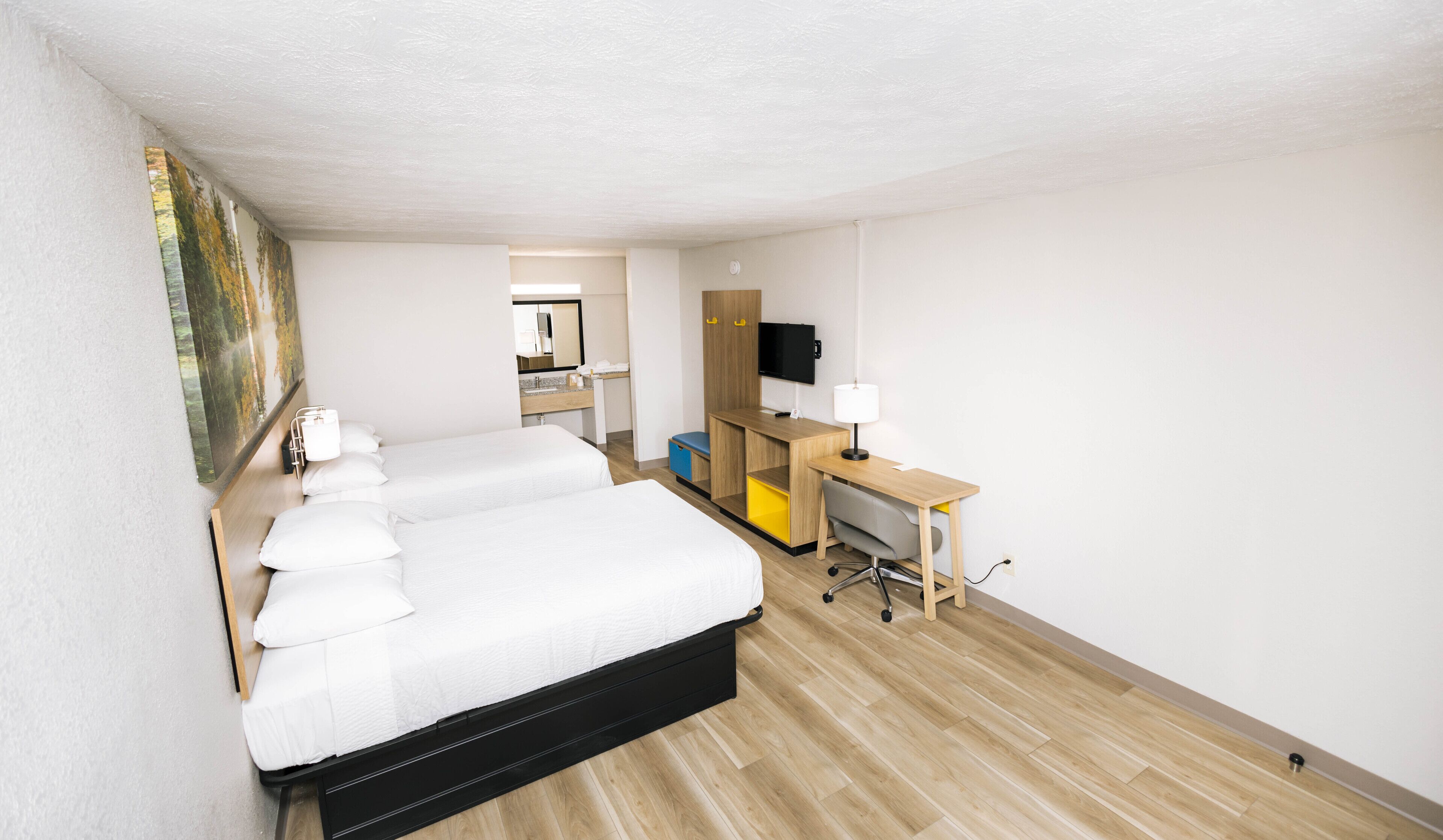 Une chambre d’hôtel avec un grand lit, un bureau avec un ordinateur, une télévision et une salle de bain visible au fond.
