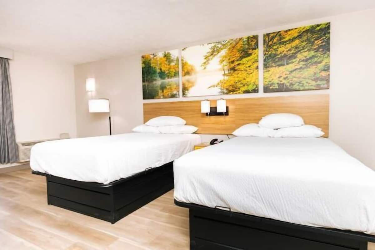 Ein Hotelzimmer mit zwei Betten, einem Holzkopfteil, einem Gemälde von Herbstlaub und einer Lampe.