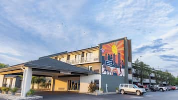 A hotel with a clear entrance, a parking lot, and a mural on the side.