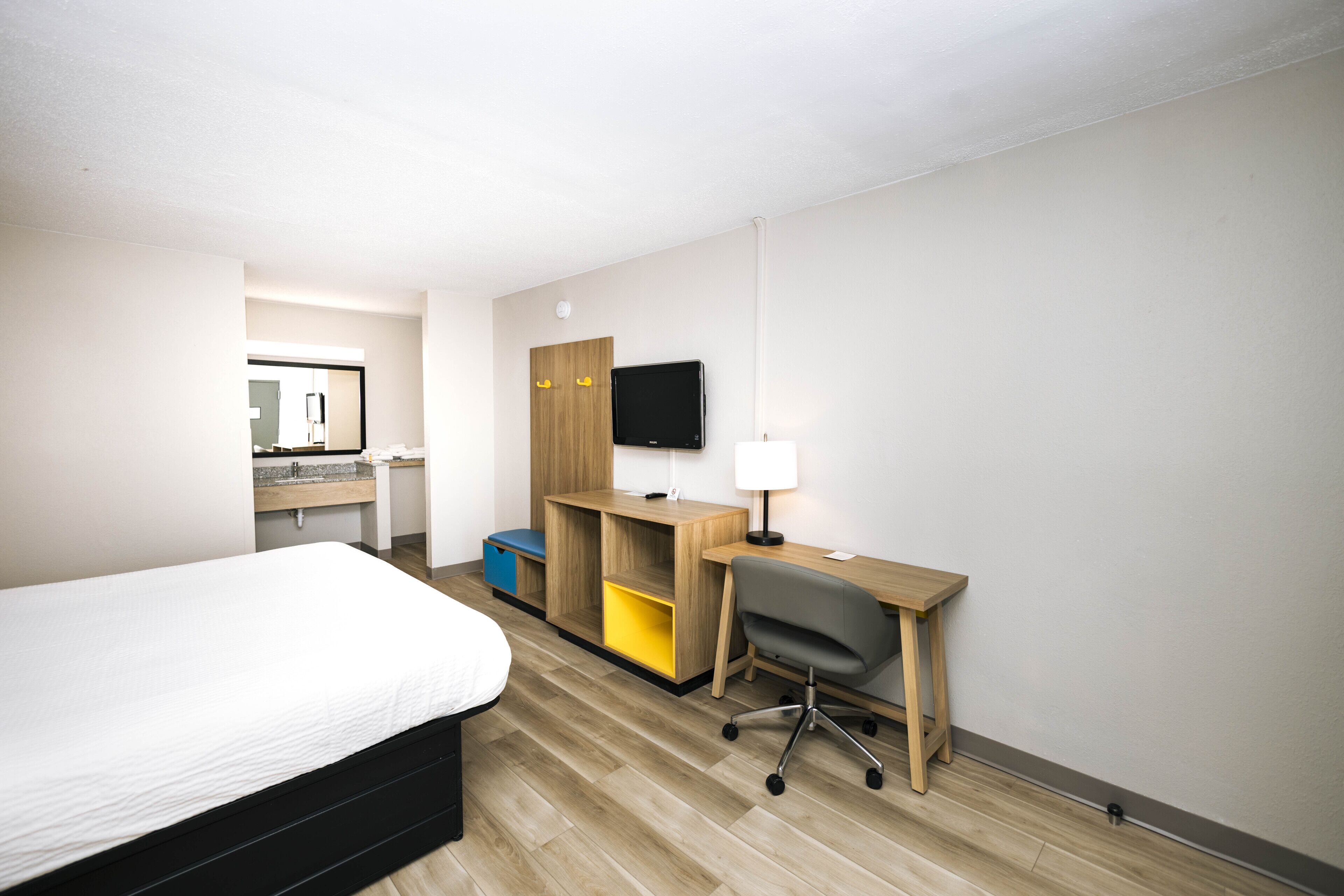 A hotel room with a bed, a desk with a chair, a television, and a mirror.