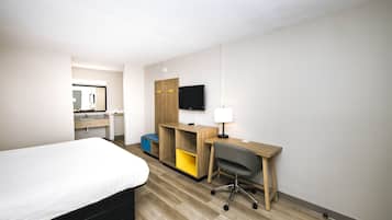 A hotel room with a bed, a desk with a chair, a television, and a mirror.