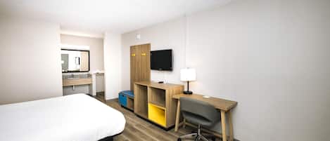 A hotel room with a bed, a desk with a chair, a television, and a mirror.