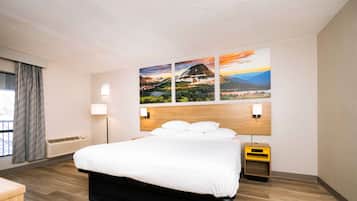 A modern hotel room with a large bed, a wooden headboard, and a wall-mounted painting.