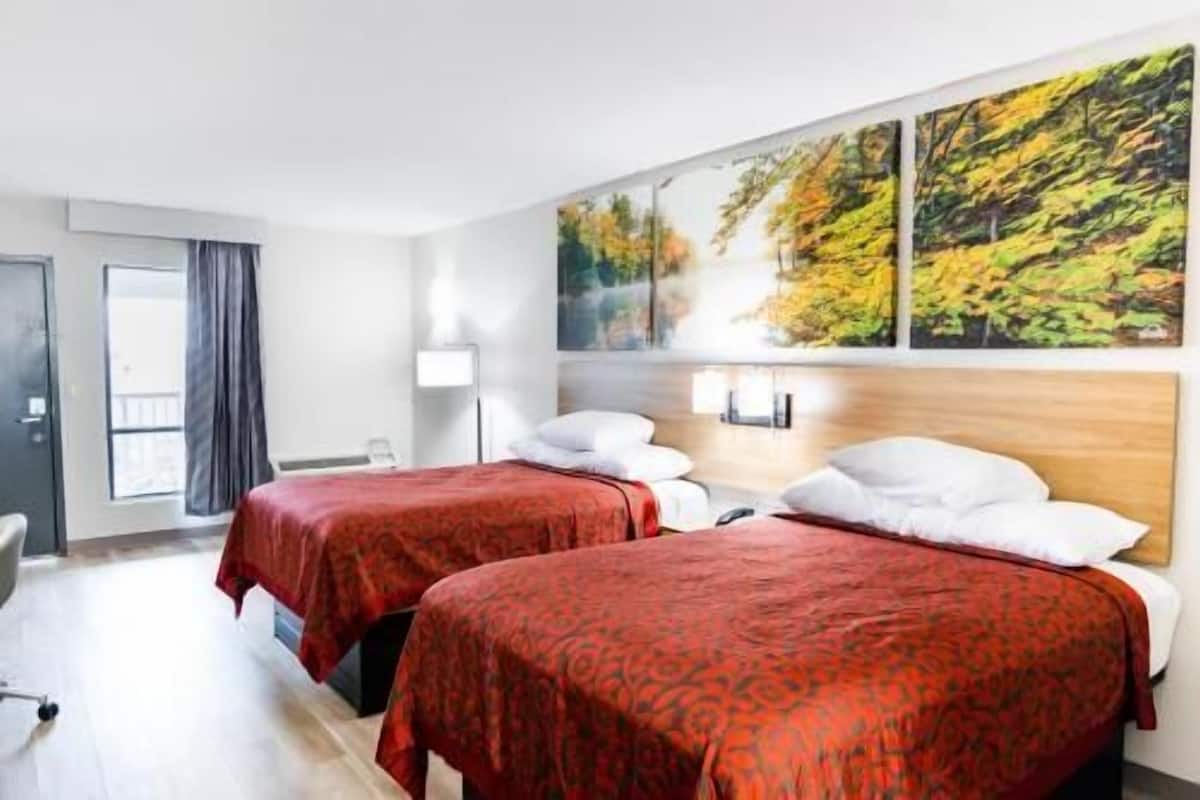 Ein Hotelzimmer mit zwei Betten, einem Schreibtisch, einem Stuhl und einem großen Fenster mit Vorhängen.
