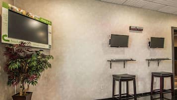 A reception area with a large flat-screen TV, two smaller monitors, a potted plant, and two bar stools.