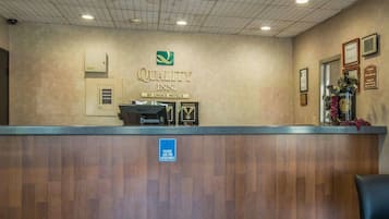 Un comptoir d'accueil dans l'hôtel Quality Inn, avec une pancarte, un ordinateur et une signalisation indiquant où obtenir de l'aide.