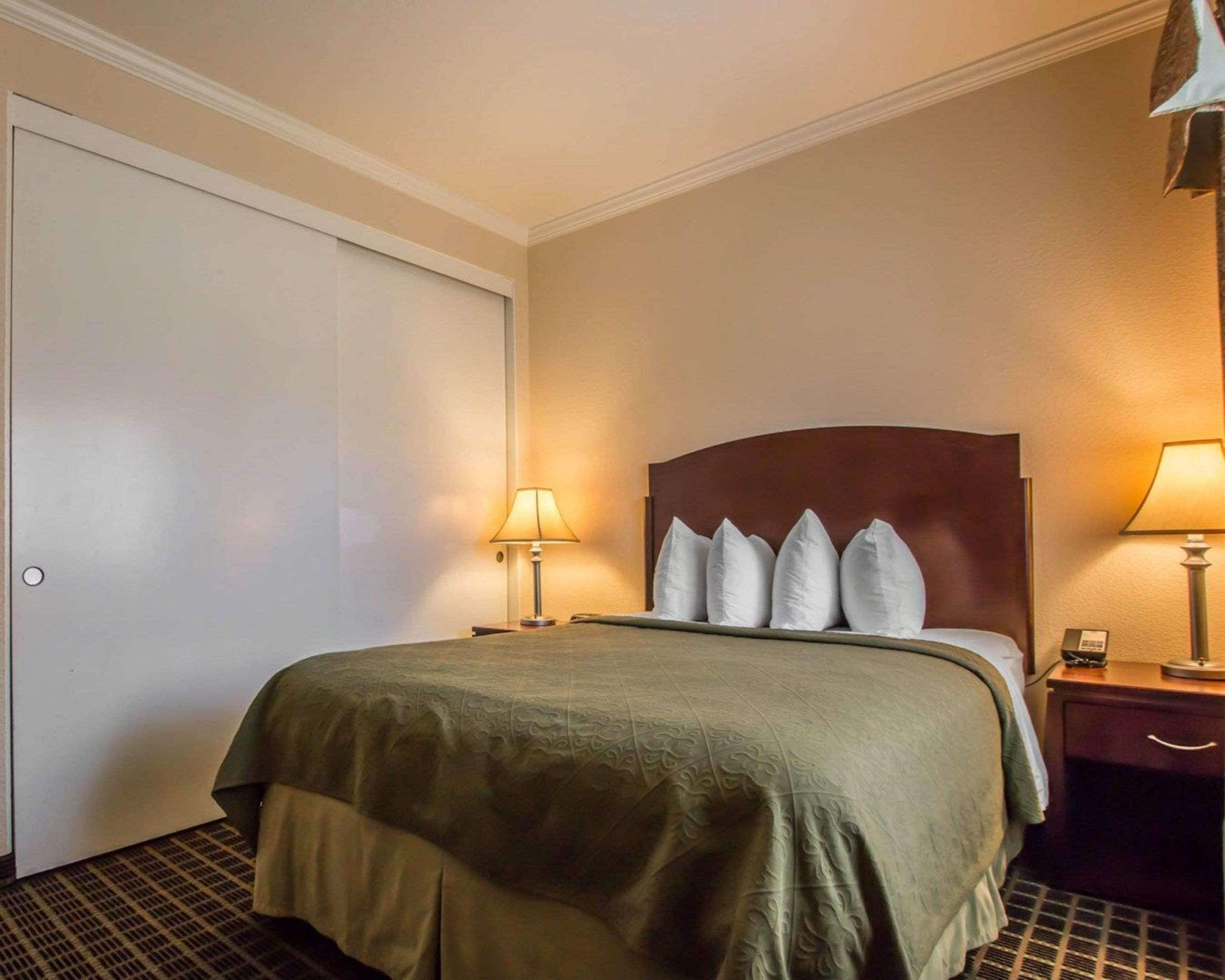 Une chambre d’hôtel avec un lit, deux lampes de chevet, une tête de lit en bois et une porte.