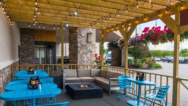 An outdoor patio with blue tables and chairs, a black fire pit, and hanging flower baskets. - Western Heritage Hotel and Conference Center, an Ascend Collection Hotel (Casper)