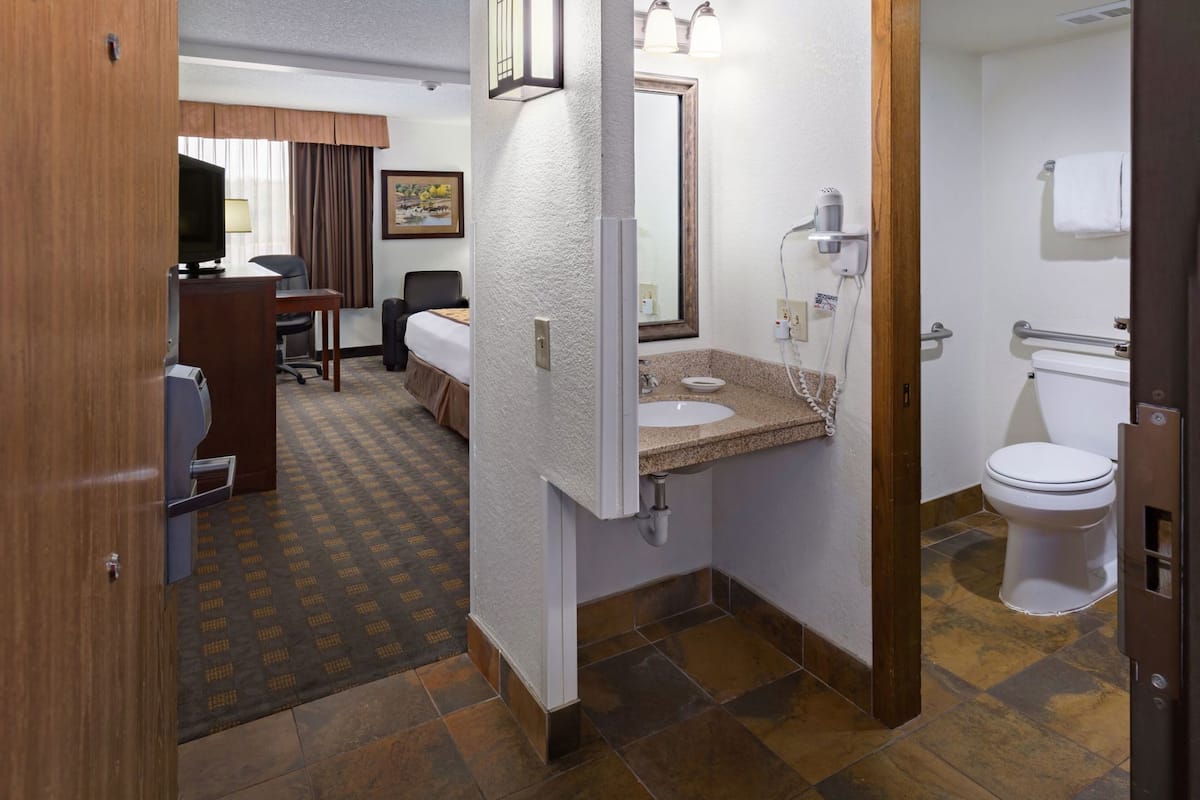 Ein Hotelzimmer mit Bett, Schreibtisch, Stuhl und einem Badezimmer mit Waschbecken, Toilette und Dusche.
