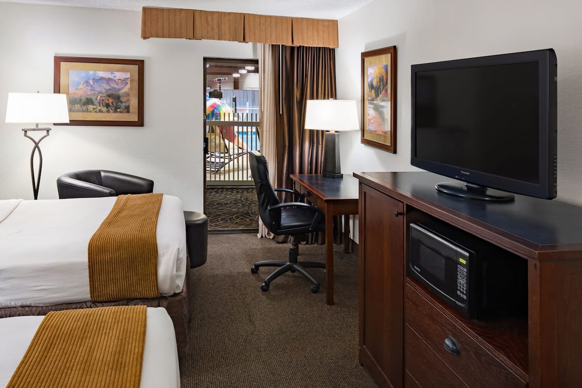 Ein Hotelzimmer mit zwei Betten, einem Schreibtisch mit Fernseher, einem Sessel, einer Lampe und einer Mikrowelle.
