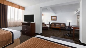 A hotel room with a bed, a TV on a wooden dresser, a sofa, a desk, and a chair. - Western Heritage Hotel and Conference Center, an Ascend Collection Hotel (Casper)