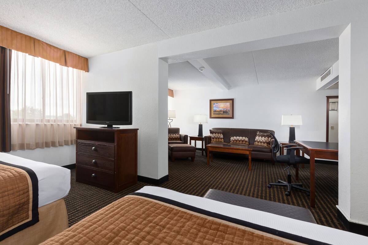 Ein Hotelzimmer mit Bett, Fernseher auf einer Holzkommode, einer Couch, einem Schreibtisch und einem Stuhl.