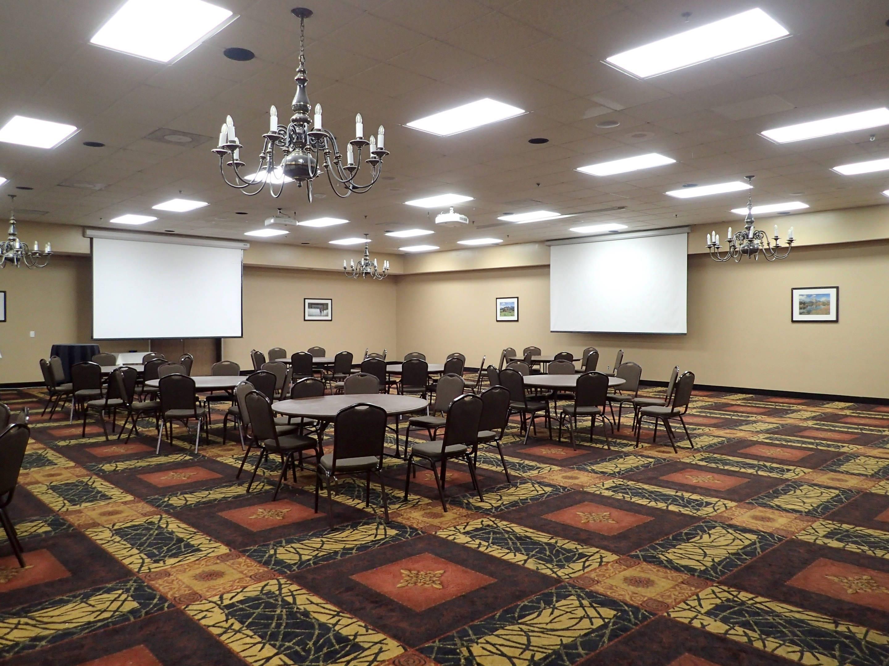 A conference room with multiple tables and chairs, a chandelier, ceiling lights, and two projection screens.