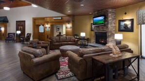 A spacious lobby with leather sofas, a fireplace, and a television mounted on the wall. - Western Heritage Hotel and Conference Center, an Ascend Collection Hotel (Casper)