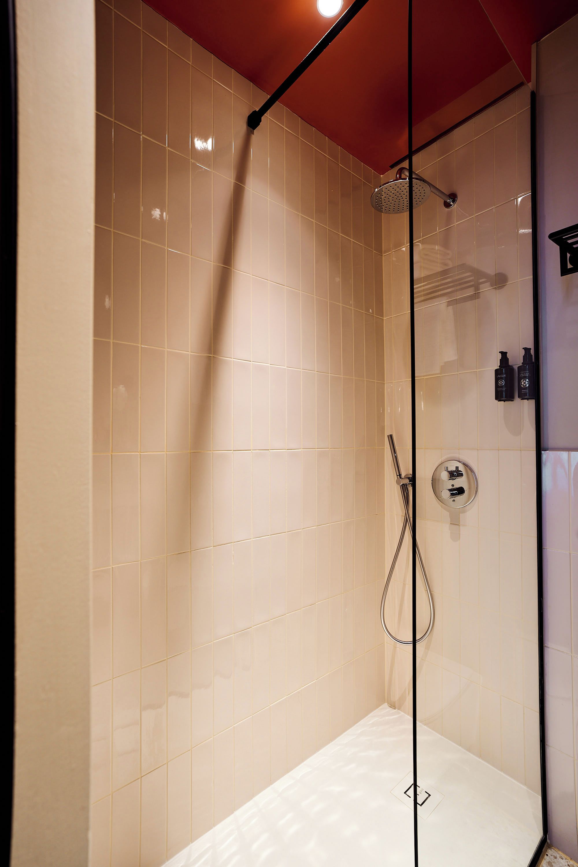 A glass-enclosed shower with a handheld showerhead and a wall-mounted faucet.