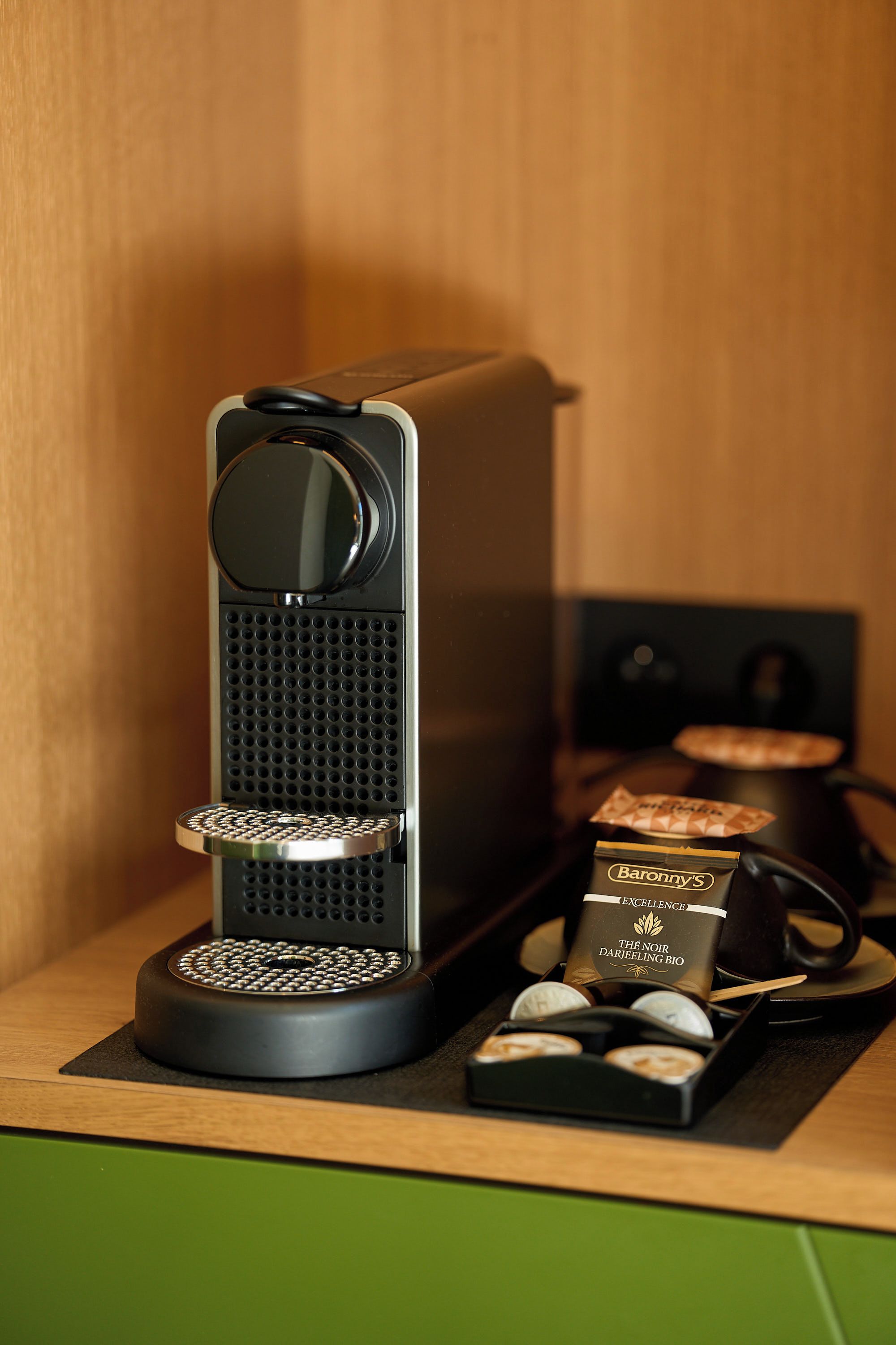 A coffee machine with a drip tray, a coffee pod, and a cup on a wooden surface.
