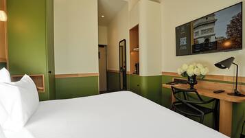 Habitación de hotel con cama, escritorio, silla, un jarrón con flores y un televisor instalado en la pared.