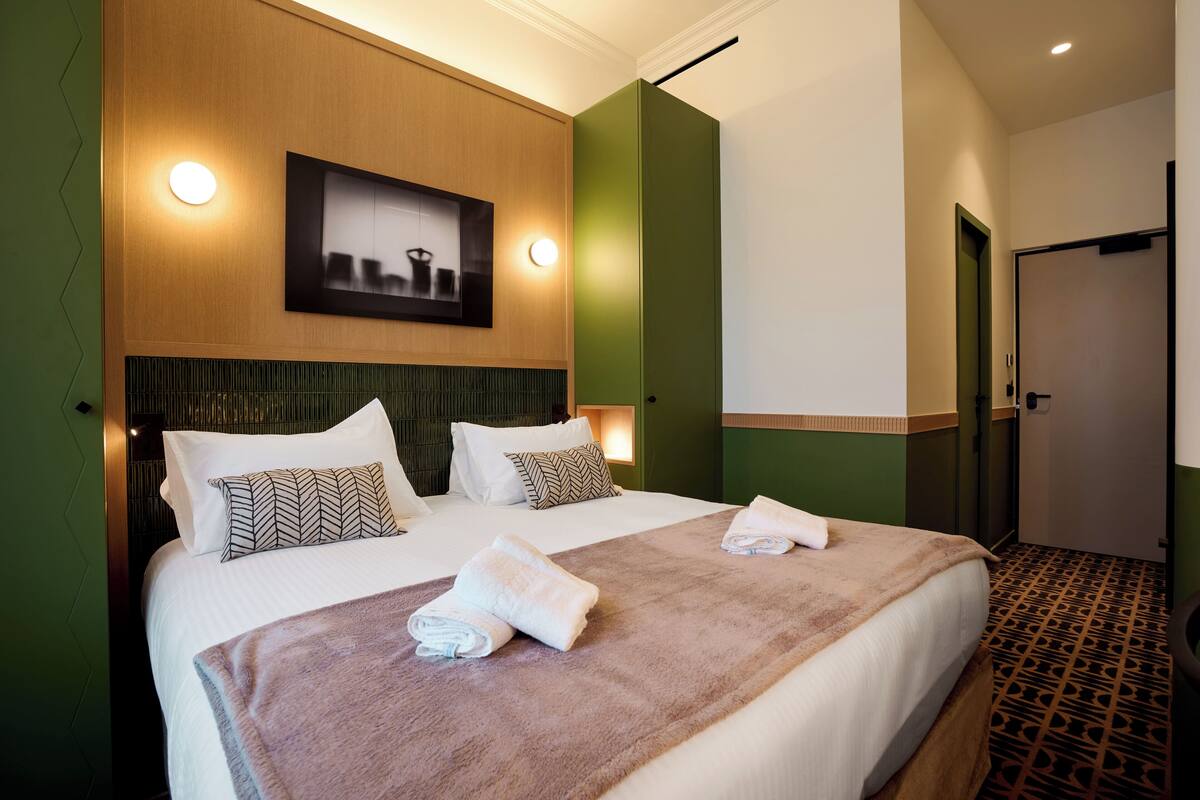 A hotel room with a large bed, two pillows, a headboard, a wall-mounted picture, and a door.
