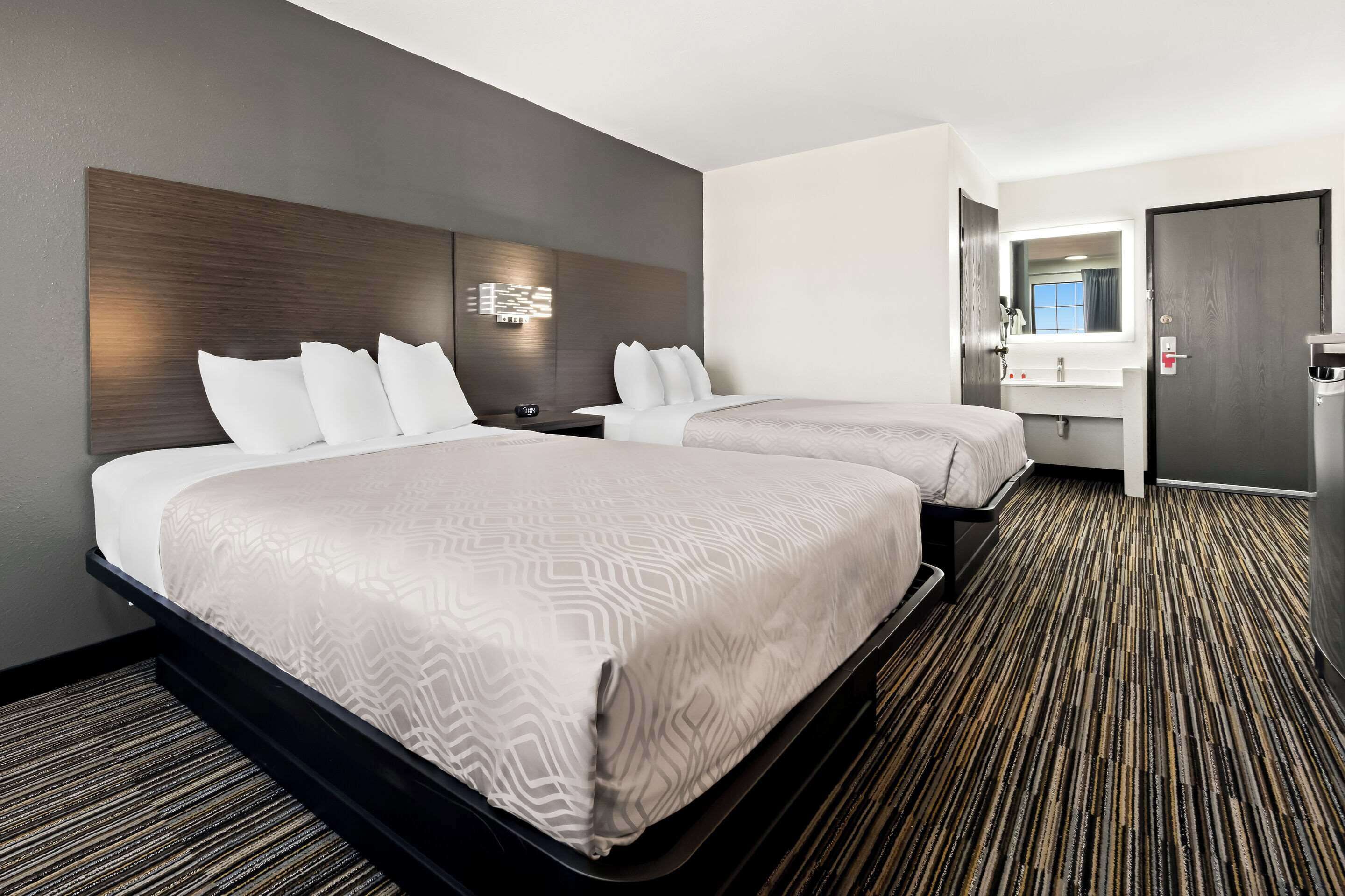 A hotel room with two beds, a bathroom with a mirror and sink, and a carpeted floor.