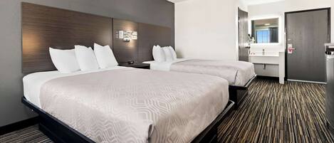 A hotel room with two beds, a bathroom with a mirror and sink, and a carpeted floor.