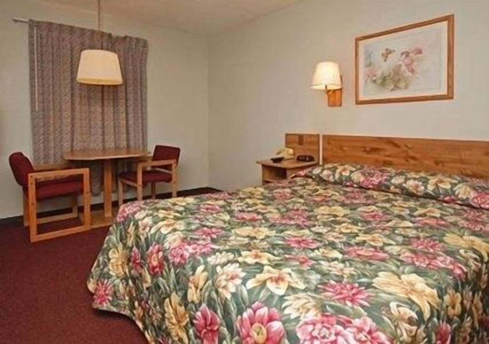 A hotel room with a bed, a desk, a chair, a lamp, and a painting on the wall.