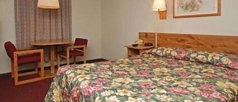 A hotel room with a bed, a desk, a chair, a lamp, and a painting on the wall.