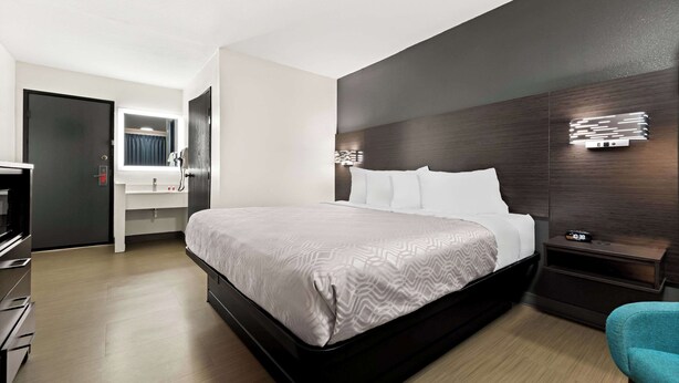 Una habitación de hotel moderna con una cama grande, una mesita de noche con un reloj, un espejo y un armario.