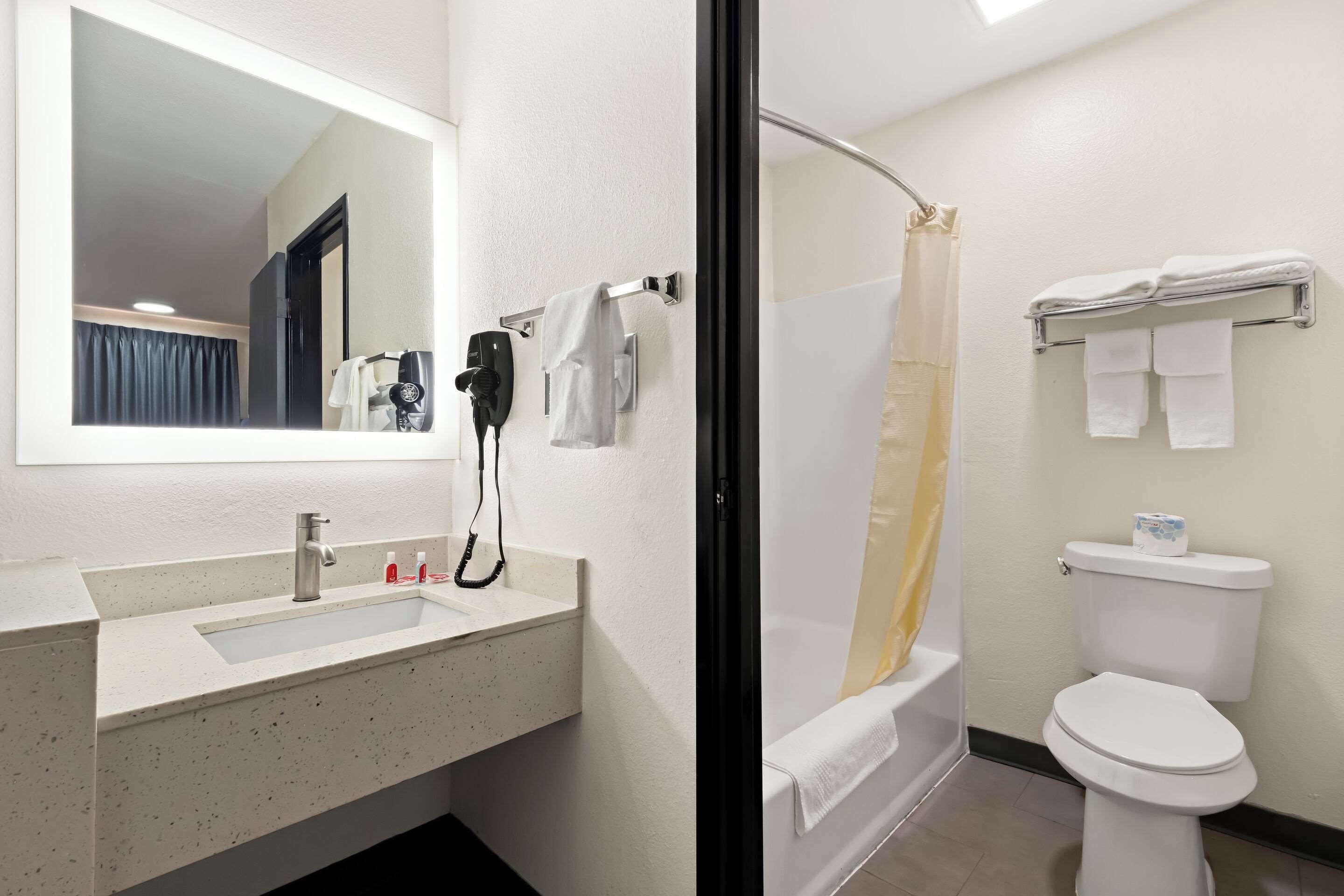 A bathroom with a sink, mirror, towel rack, shower, and toilet.
