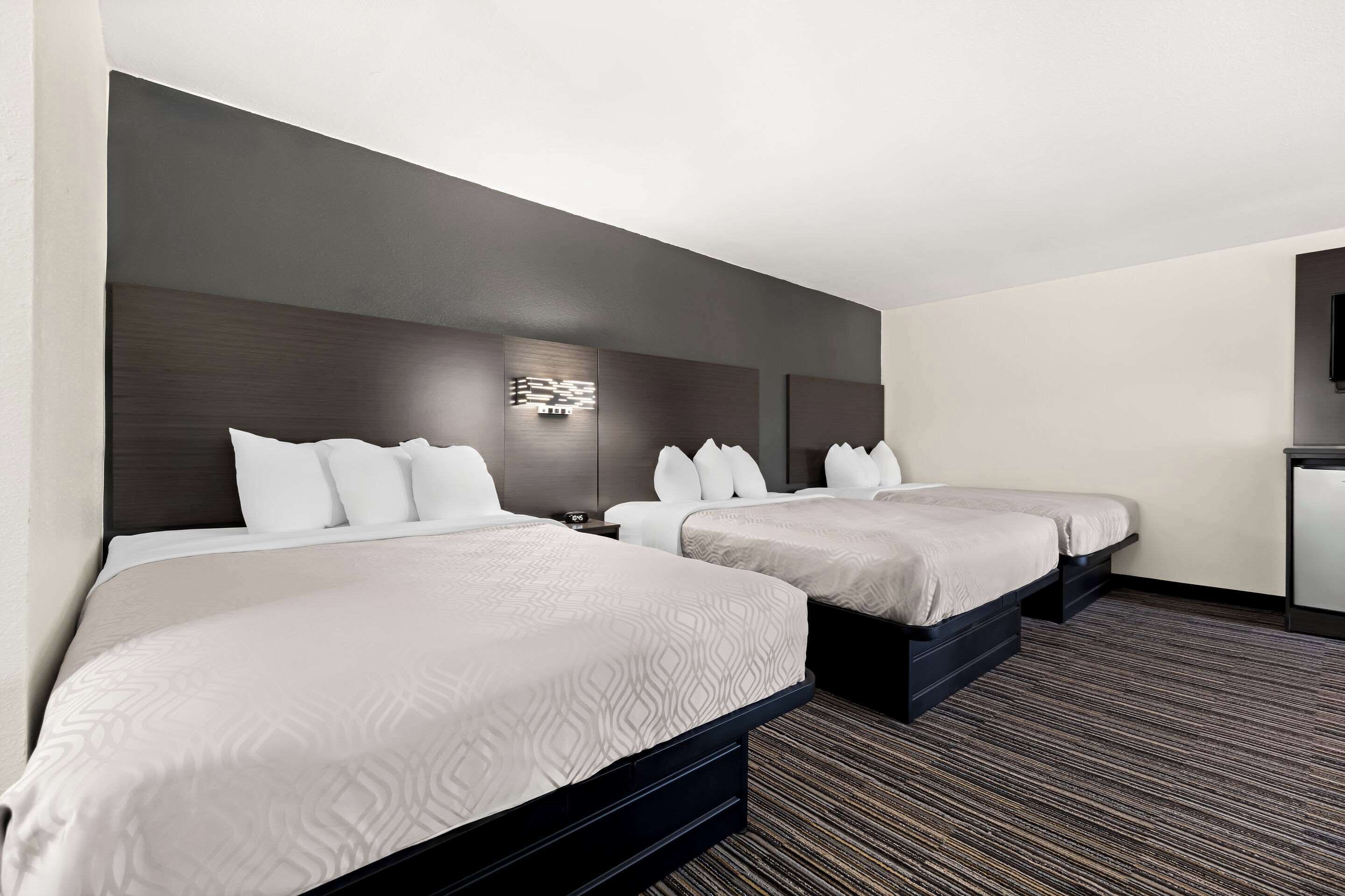 A hotel room with two beds, a dark headboard, a wall-mounted light, and a carpeted floor.