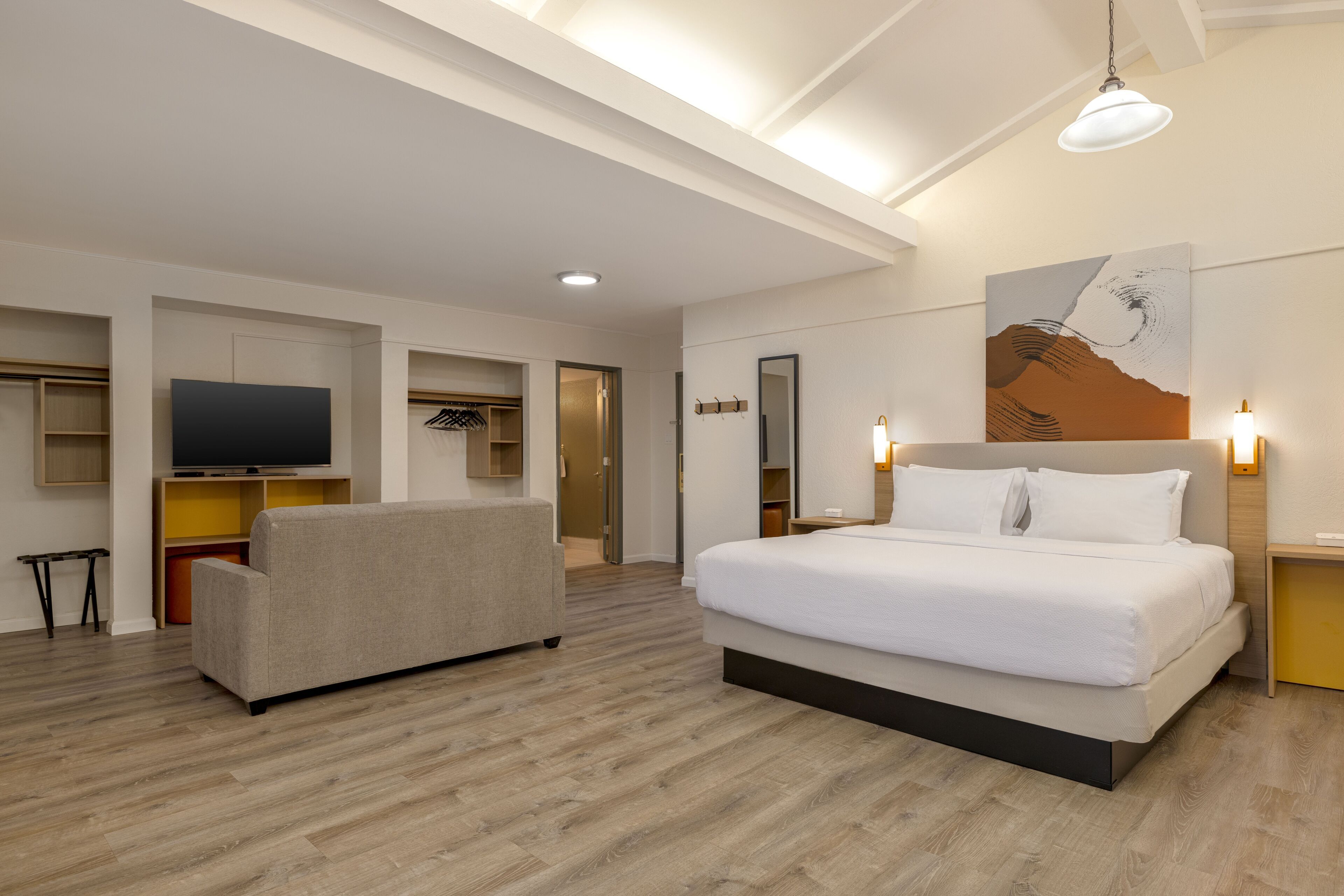 A hotel room with a bed, a TV, a sofa, and a painting on the wall.