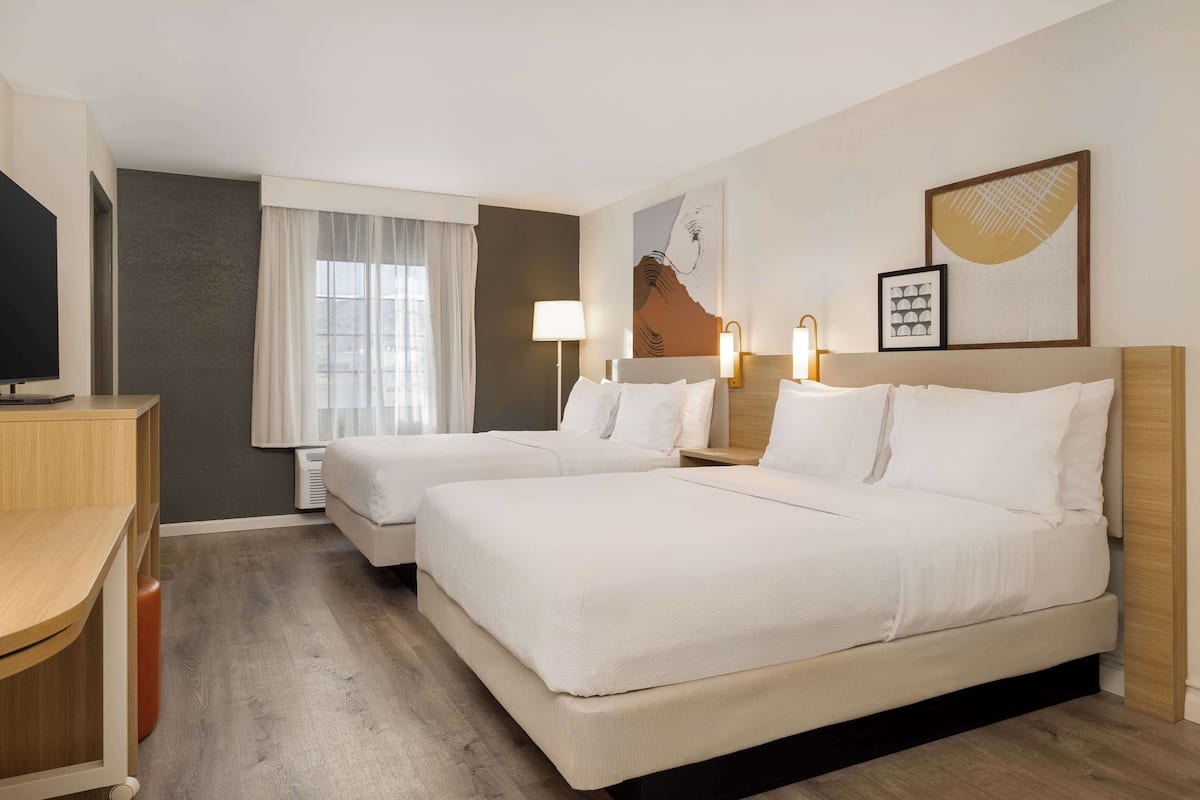 A hotel room with two beds, a desk, and a TV.