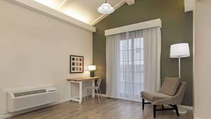 A modern room with a wooden floor, a desk with a chair, a lamp, a radiator, and a large window with curtains. - Spark by Hilton Rock Springs (Rock Springs)