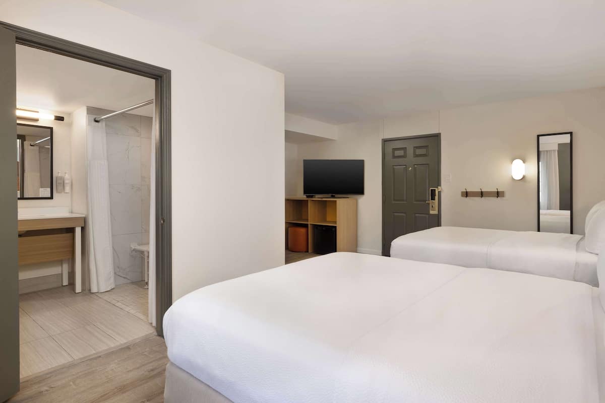 A hotel room with two beds, a TV, a bathroom with a shower, and a desk.
